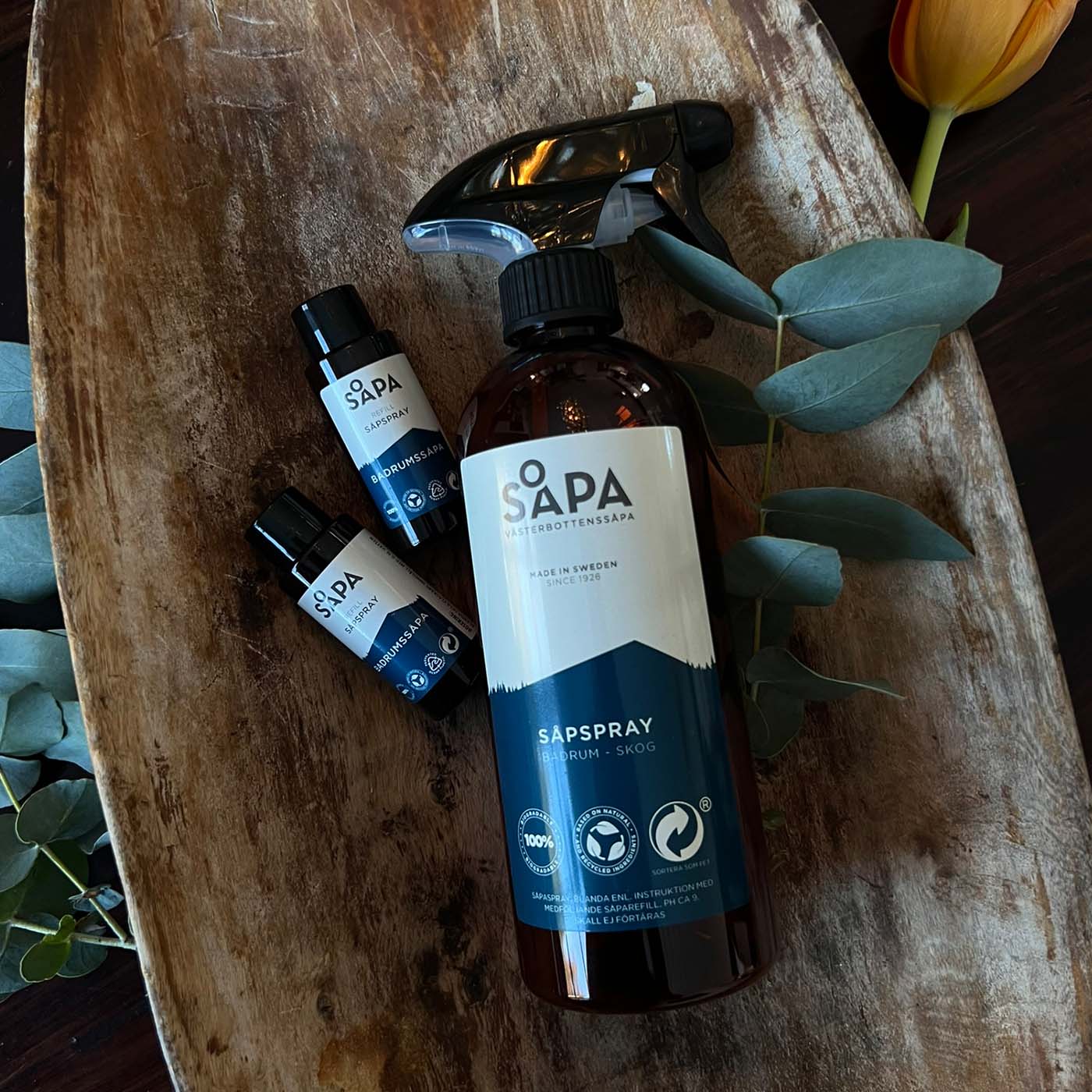 Naturlig och effektiv såpspray och två refiller med doft av skog placerad i en rustik trälåda.