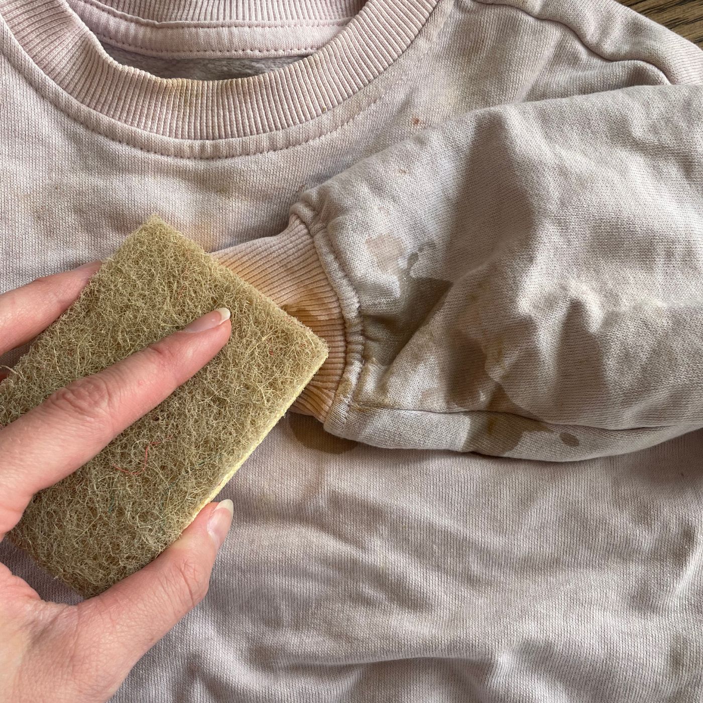 En bild som visar en smutsig tröja och en cellulosasvamp. Ta bort smuts med hjälp av såpa - utan starka kemikalier, skonsamt för tyget.