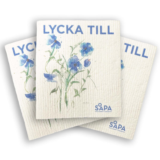 3-pack budskapstrasor med texten 'Lycka till' och blå blommor. Miljövänliga disktrasor från Västerbottenssåpa, hållbar design för ett mer naturligt hem.